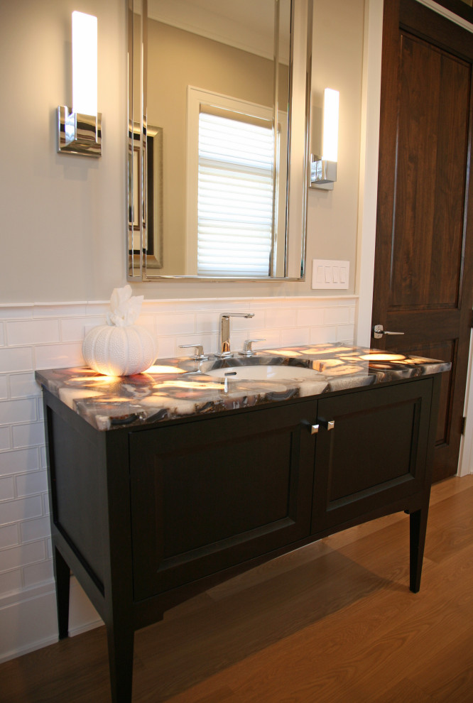 Inspiration for a mid-sized transitional white tile and ceramic tile light wood floor, brown floor and wainscoting powder room remodel in Milwaukee with recessed-panel cabinets, dark wood cabinets, a two-piece toilet, gray walls, an undermount sink, onyx countertops, brown countertops and a freestanding vanity