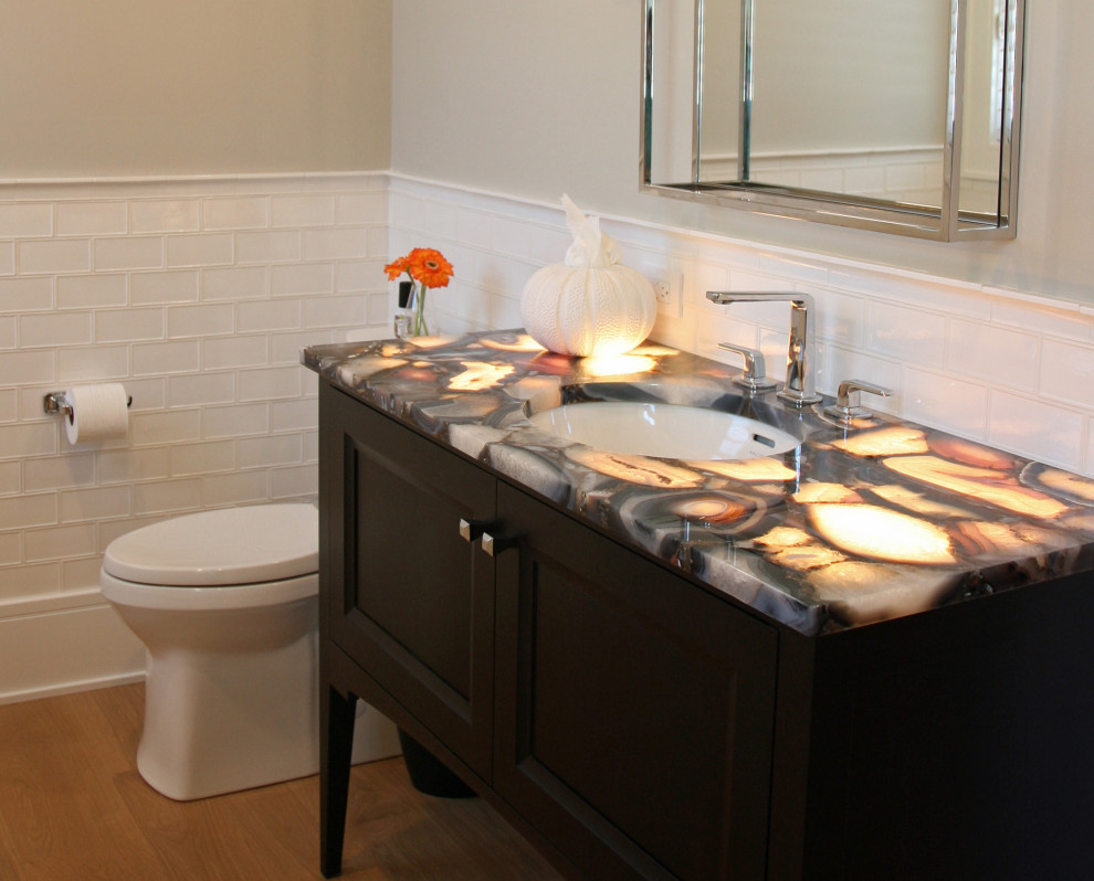Powder room - mid-sized transitional white tile and ceramic tile light wood floor, brown floor and wainscoting powder room idea in Milwaukee with recessed-panel cabinets, dark wood cabinets, a two-piece toilet, gray walls, an undermount sink, onyx countertops, brown countertops and a freestanding vanity