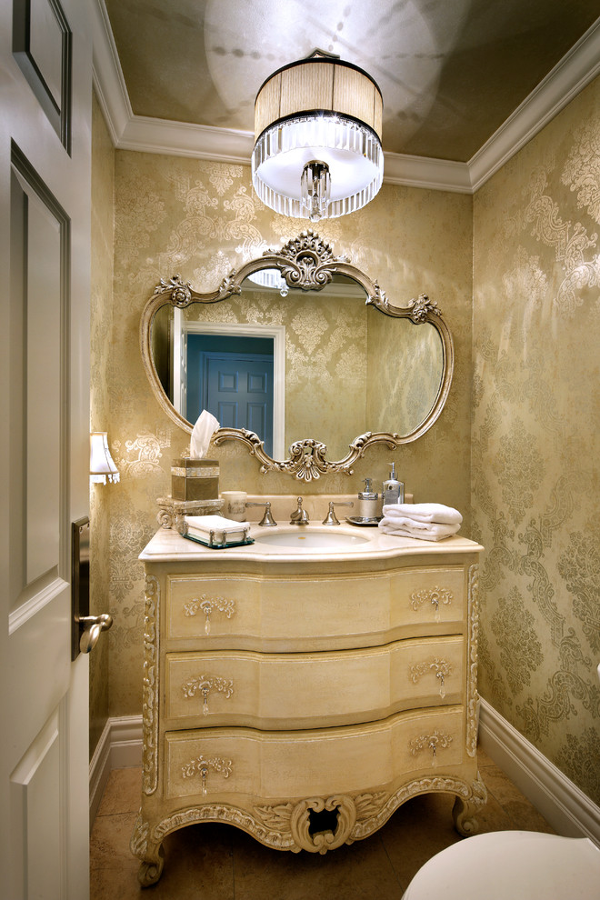 Idee per un piccolo bagno di servizio chic con consolle stile comò, ante beige, WC a due pezzi, piastrelle beige, pavimento in travertino, lavabo sottopiano, top in marmo e pareti gialle