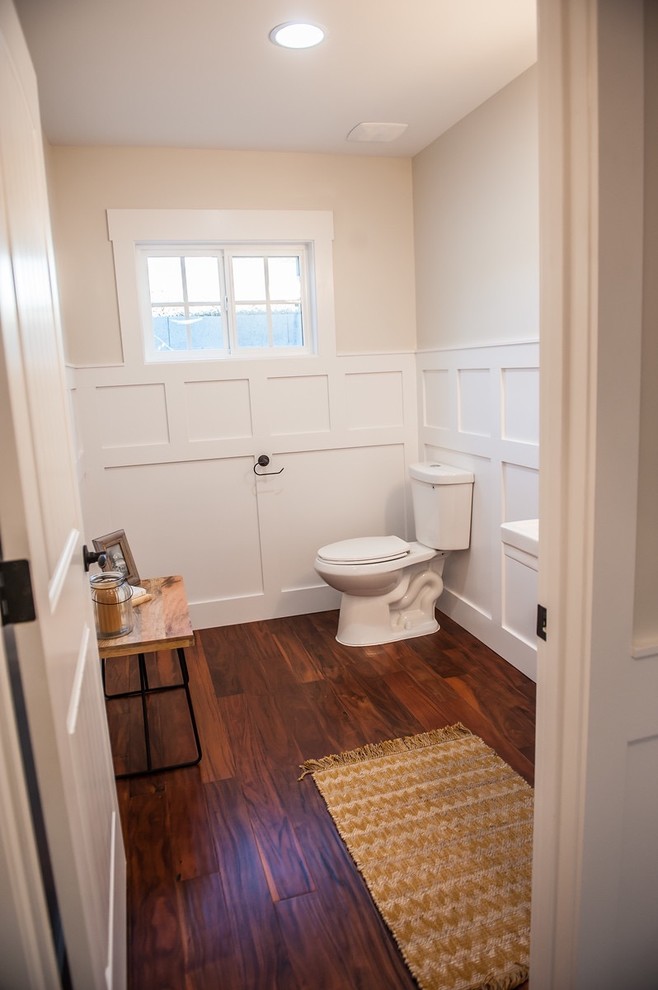 Foto på ett stort amerikanskt toalett, med ett piedestal handfat, mörkt trägolv, en toalettstol med separat cisternkåpa och beige väggar