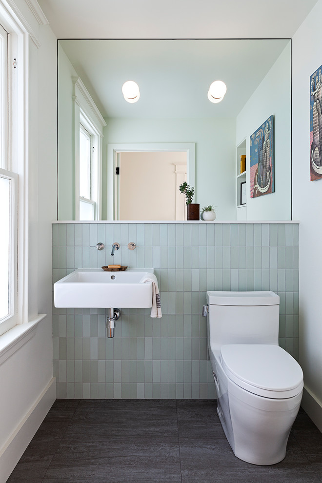 Inredning av ett modernt toalett, med öppna hyllor, en toalettstol med hel cisternkåpa, grön kakel, tunnelbanekakel, vita väggar, mörkt trägolv, ett väggmonterat handfat och svart golv