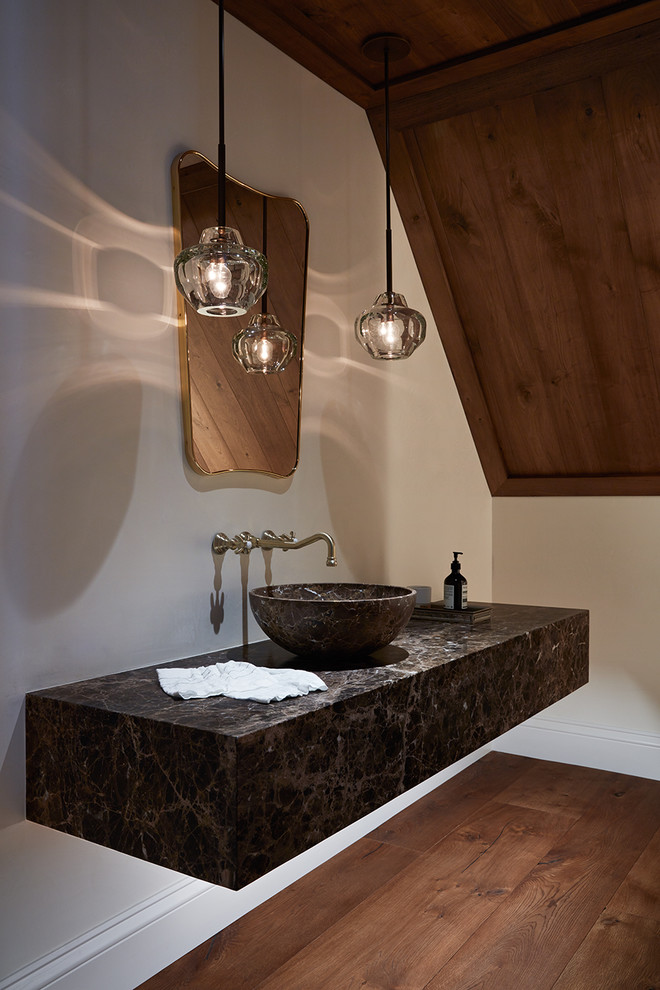 Modelo de aseo flotante actual con paredes blancas, suelo de madera en tonos medios, lavabo sobreencimera, suelo marrón, puertas de armario negras y madera