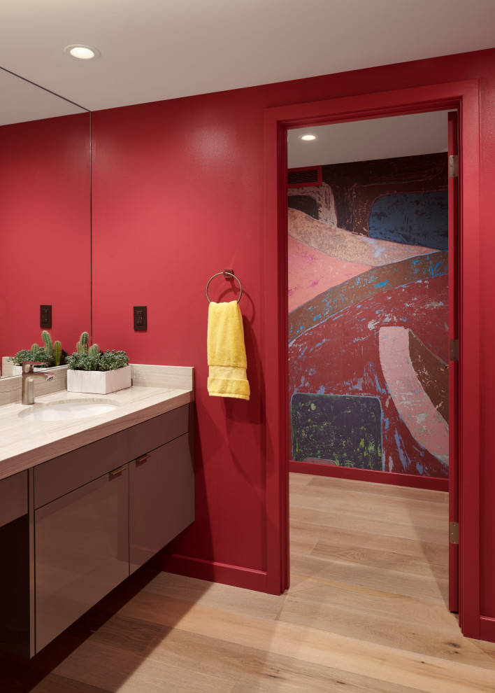 Example of a large trendy light wood floor and wallpaper powder room design in San Francisco with flat-panel cabinets, brown cabinets, pink walls, marble countertops, beige countertops and a floating vanity