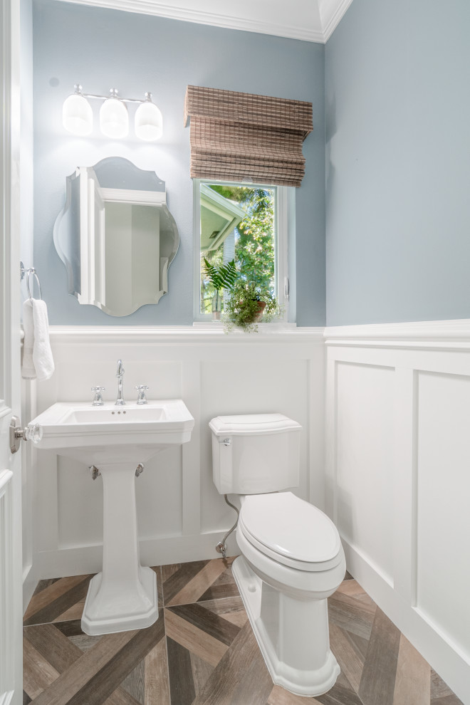 マイアミにあるお手頃価格の小さなトランジショナルスタイルのおしゃれなトイレ・洗面所 (青い壁、磁器タイルの床、茶色い床、白い洗面カウンター、分離型トイレ、ペデスタルシンク、羽目板の壁) の写真