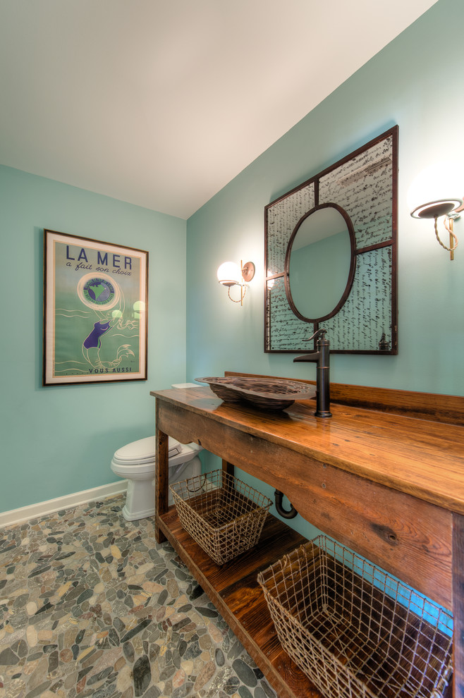 Cette photo montre un WC et toilettes bord de mer en bois brun de taille moyenne avec un placard sans porte, WC séparés, un sol en galet, une vasque, un plan de toilette en bois, un mur vert, un sol multicolore et un plan de toilette marron.