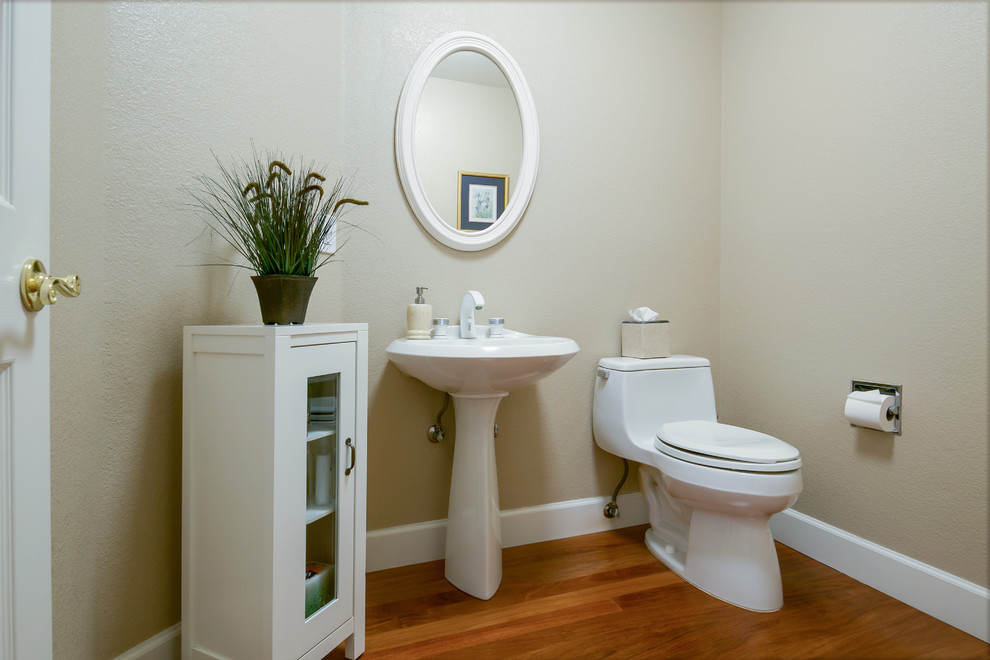 Cette image montre un WC et toilettes traditionnel de taille moyenne avec un placard à porte vitrée, WC à poser, un mur beige, parquet foncé, un lavabo de ferme et un sol marron.