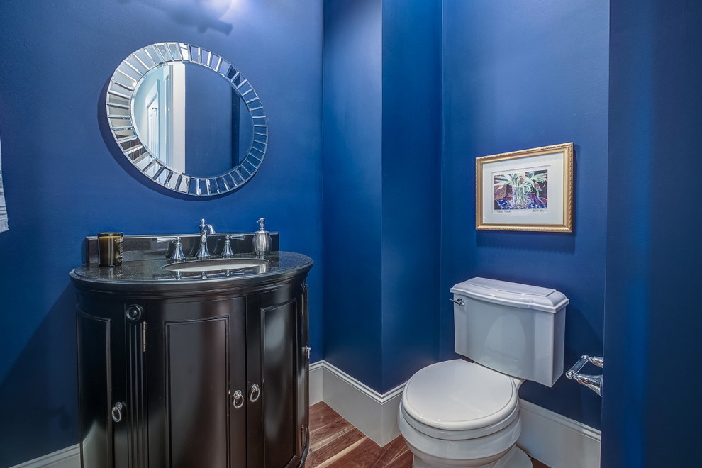 Idées déco pour un petit WC et toilettes classique avec un placard en trompe-l'oeil, des portes de placard noires, un mur bleu, un sol en bois brun, un lavabo encastré et un plan de toilette en granite.
