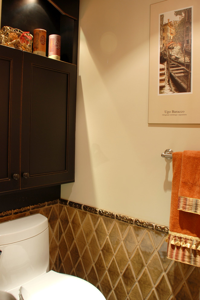 Klassisk inredning av ett litet toalett, med ett fristående handfat, luckor med infälld panel, marmorbänkskiva, en toalettstol med hel cisternkåpa, keramikplattor, vita väggar, skåp i slitet trä och brun kakel