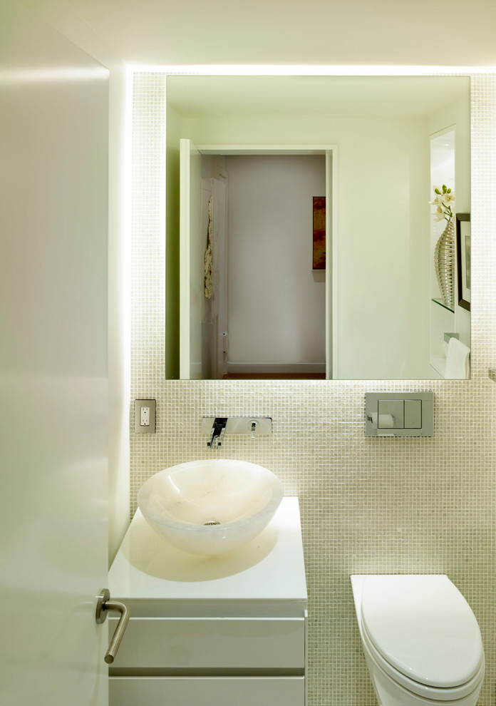 На фото: туалет среднего размера в современном стиле с стеклянной плиткой, настольной раковиной, плоскими фасадами, белыми фасадами, мраморной столешницей и инсталляцией с