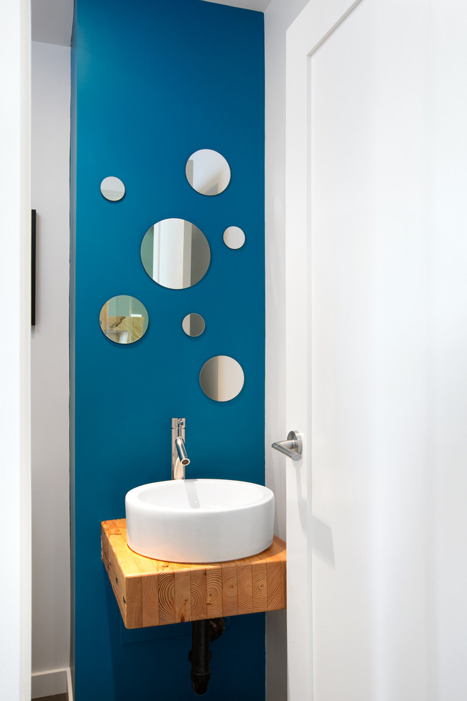 На фото: туалет в современном стиле с настольной раковиной, столешницей из дерева, синими стенами и коричневой столешницей
