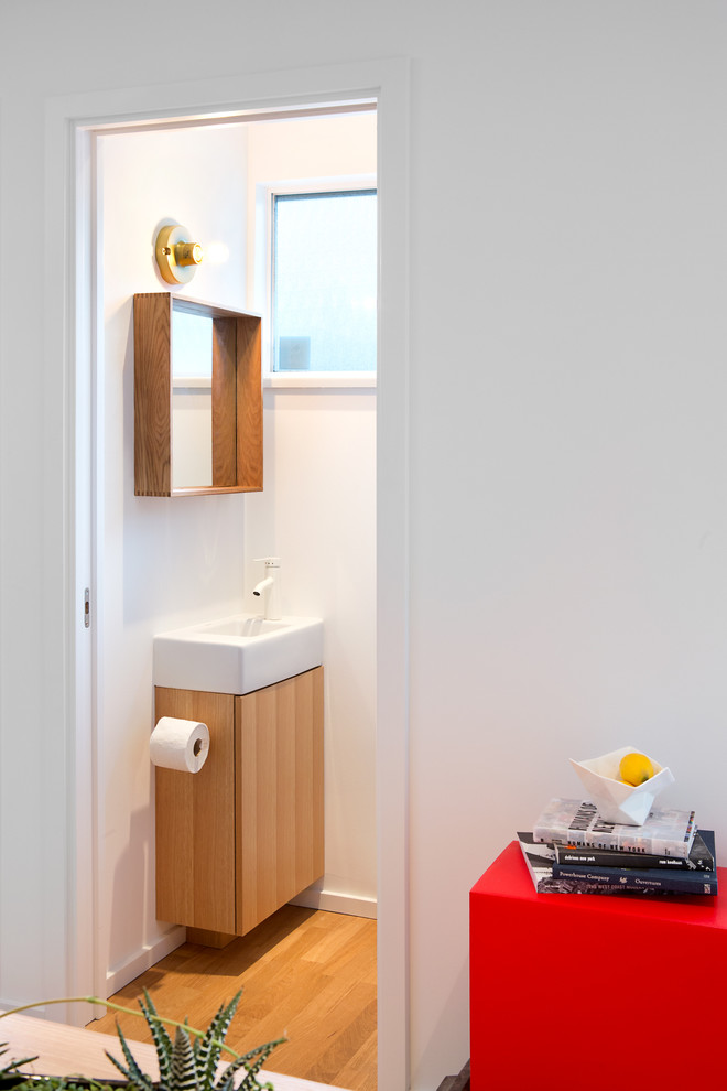 Ispirazione per un bagno di servizio moderno di medie dimensioni con lavabo sospeso, ante lisce, ante in legno scuro, WC monopezzo, pareti bianche e pavimento in legno massello medio
