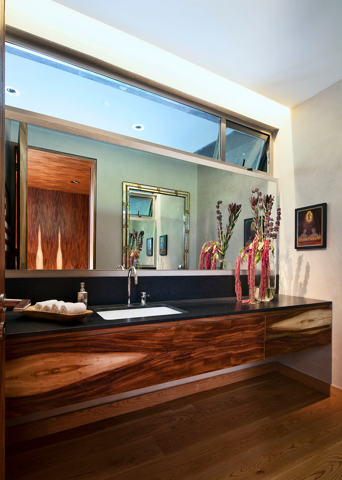 Moderne Gästetoilette mit Unterbauwaschbecken, flächenbündigen Schrankfronten, hellbraunen Holzschränken und schwarzer Waschtischplatte in Mexiko Stadt