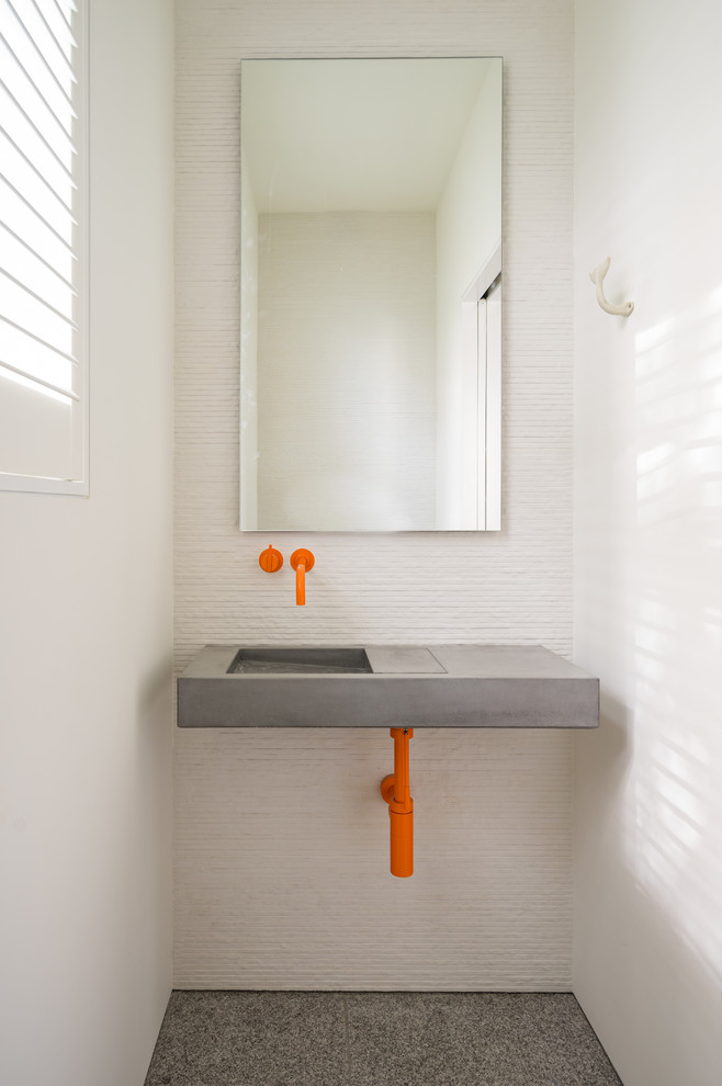 Inredning av ett maritimt litet toalett, med vita väggar, ett väggmonterat handfat, bänkskiva i betong och grått golv