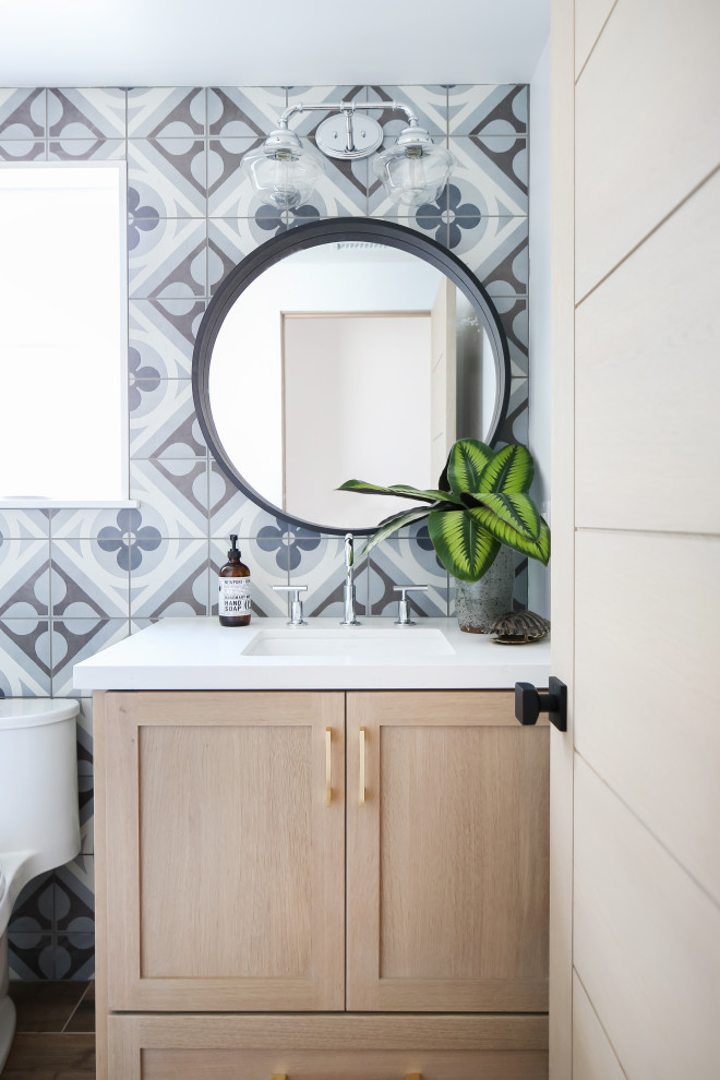 Inspiration for a coastal blue tile, gray tile and white tile wood-look tile floor and brown floor powder room remodel in Orange County with shaker cabinets, light wood cabinets, a one-piece toilet, blue walls, an undermount sink, white countertops and a built-in vanity