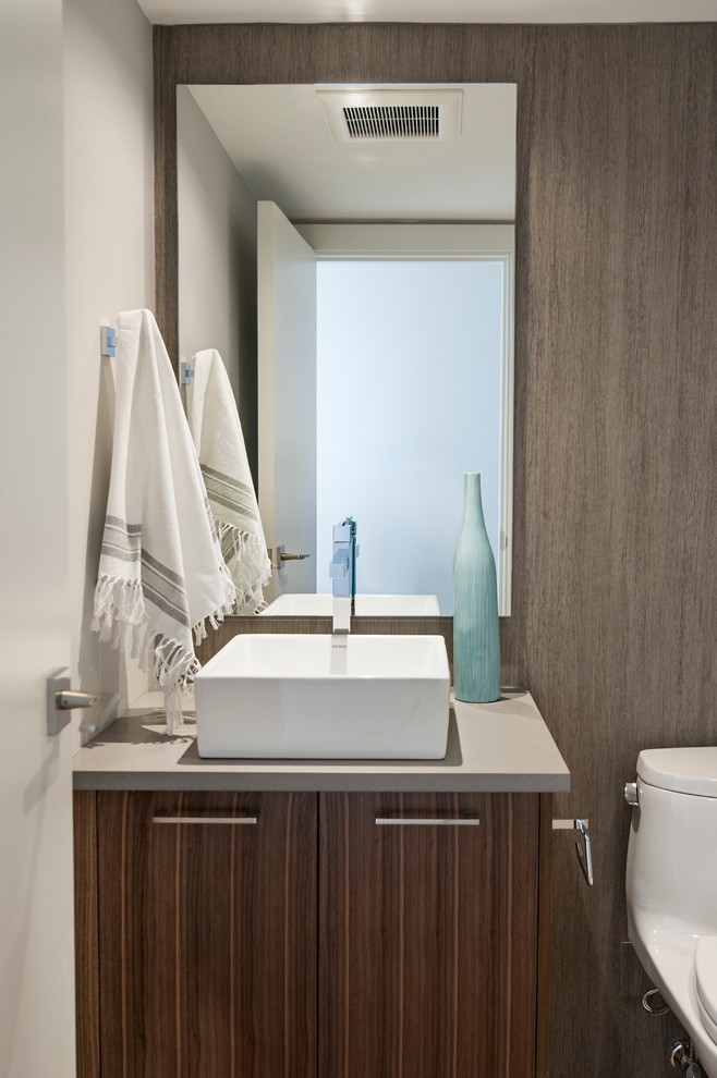 Design ideas for a small contemporary cloakroom in Vancouver with flat-panel cabinets, a one-piece toilet, grey tiles, porcelain tiles, grey walls, a vessel sink, engineered stone worktops, medium wood cabinets, light hardwood flooring, brown floors and grey worktops.