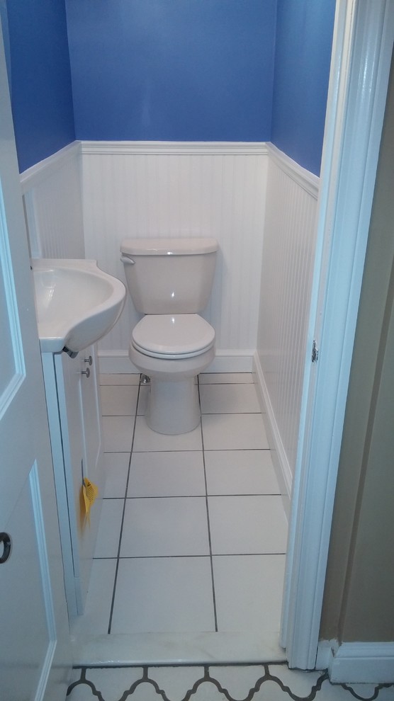 Exemple d'un petit WC et toilettes chic avec un placard avec porte à panneau surélevé, des portes de placard blanches, WC séparés, un carrelage blanc, des carreaux de porcelaine, un mur bleu, un sol en carrelage de porcelaine, un lavabo intégré et un plan de toilette en surface solide.