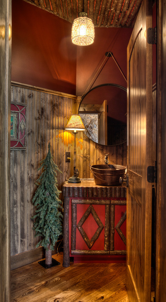 Urige Gästetoilette mit Aufsatzwaschbecken, braunem Holzboden, verzierten Schränken und roter Wandfarbe in Minneapolis
