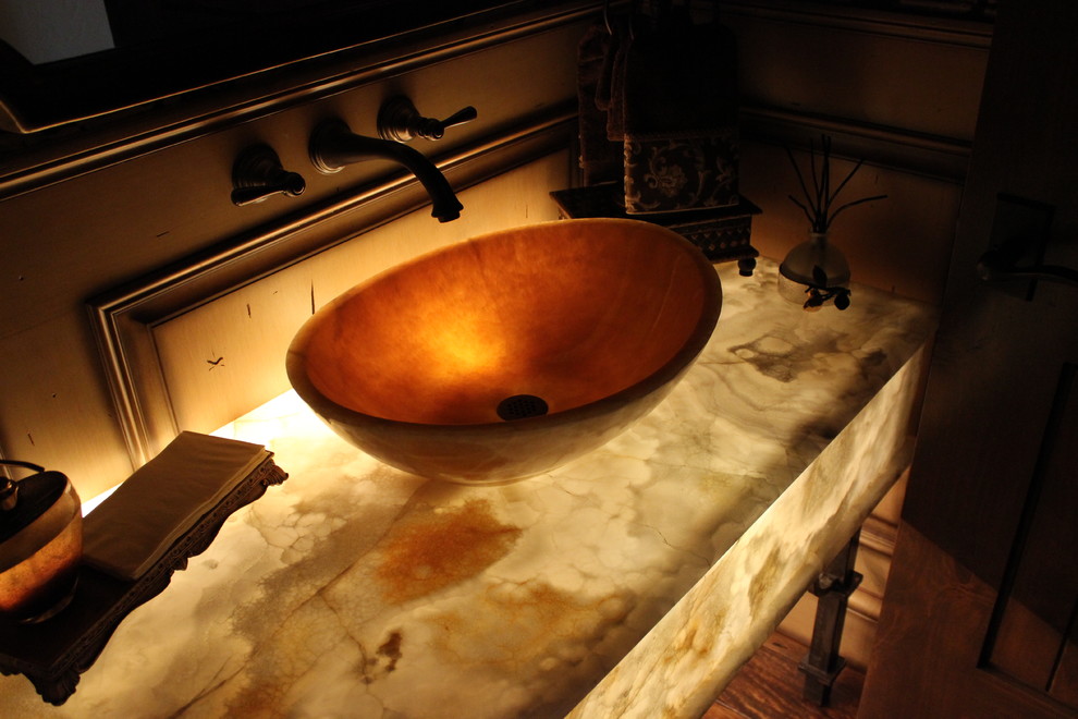 Inredning av ett klassiskt mellanstort toalett, med ett fristående handfat, bänkskiva i onyx, vit kakel, bruna väggar och mörkt trägolv
