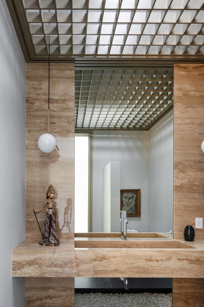 Cette image montre un WC et toilettes design avec un carrelage beige, des dalles de pierre, un mur gris, un lavabo intégré et un plan de toilette beige.