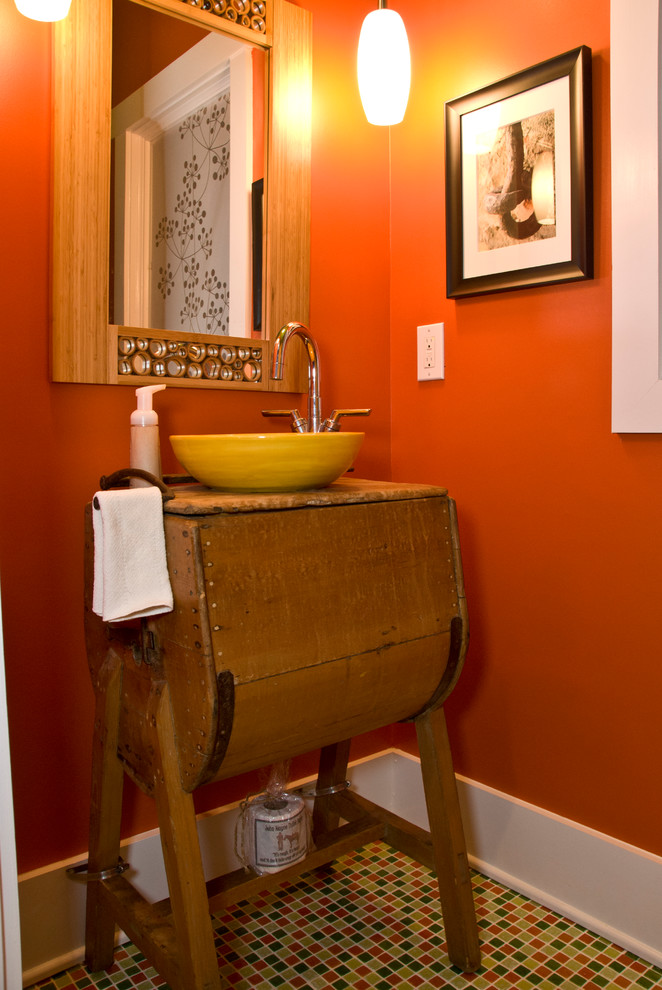 Kleine Eklektische Gästetoilette mit verzierten Schränken, hellbraunen Holzschränken, oranger Wandfarbe, Mosaik-Bodenfliesen, Aufsatzwaschbecken, Waschtisch aus Holz und buntem Boden in Charlotte