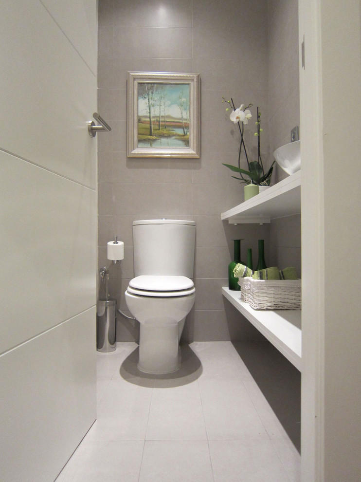Modern inredning av ett litet toalett, med öppna hyllor, vita skåp, en toalettstol med separat cisternkåpa, grå väggar, klinkergolv i keramik och ett fristående handfat