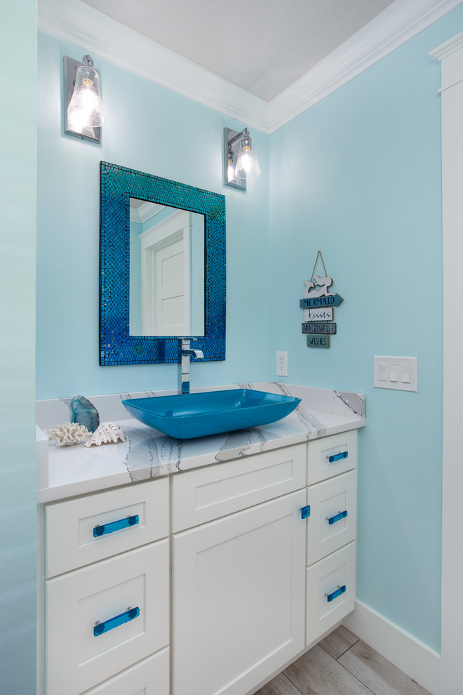 Aménagement d'un petit WC et toilettes bord de mer avec un placard à porte shaker, des portes de placard blanches, un mur bleu, une vasque, un plan de toilette en quartz modifié et un plan de toilette blanc.
