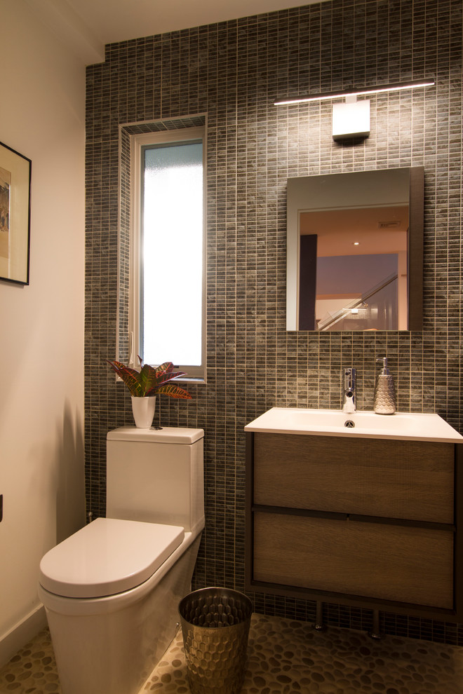 Design ideas for a small modern cloakroom in New York with flat-panel cabinets, medium wood cabinets, a one-piece toilet, multi-coloured tiles, porcelain tiles, white walls, pebble tile flooring, an integrated sink, solid surface worktops, beige floors and white worktops.