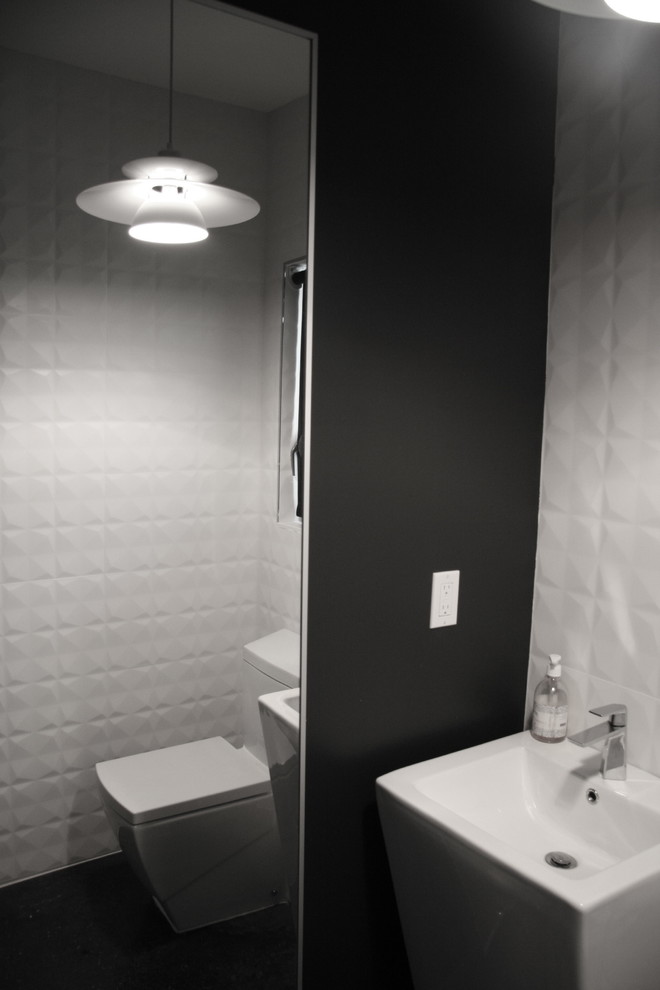Inredning av ett modernt litet toalett, med ett piedestal handfat, en toalettstol med hel cisternkåpa, vit kakel, porslinskakel, svarta väggar och betonggolv