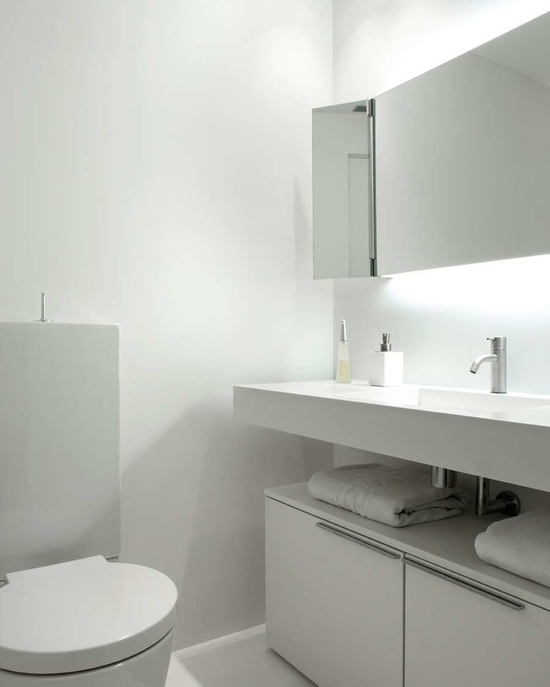 Cette image montre un petit WC et toilettes design avec un placard à porte plane, WC séparés, un mur blanc et un lavabo intégré.
