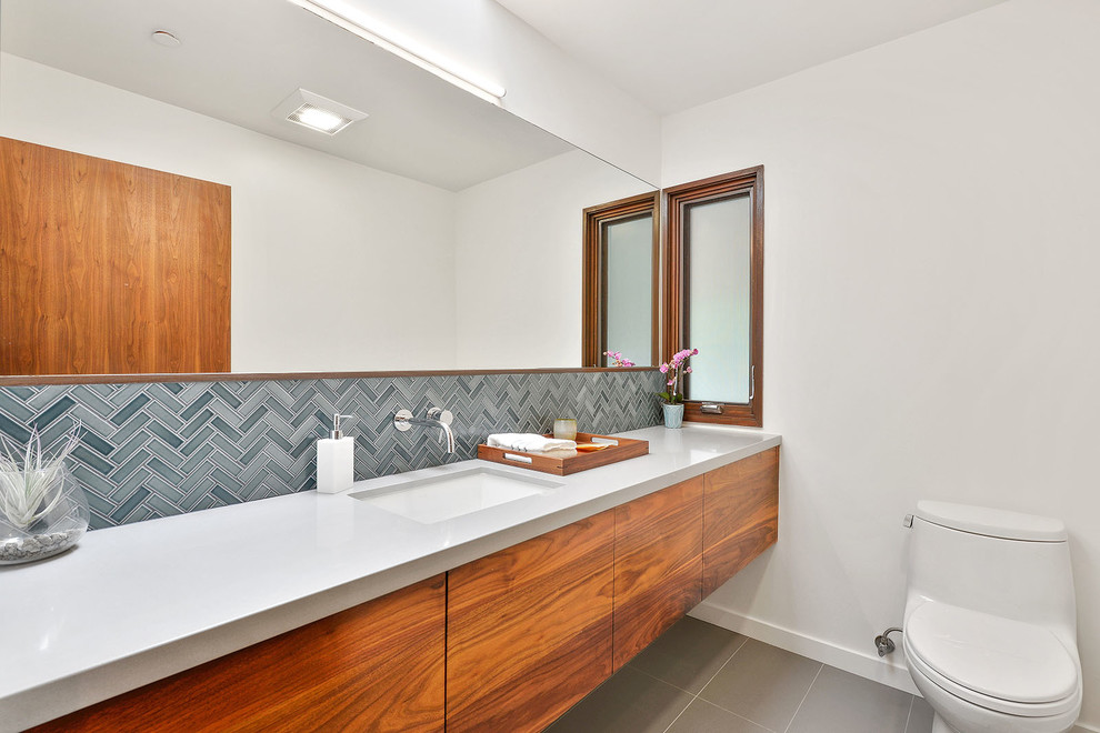 Example of a trendy gray tile and porcelain tile porcelain tile powder room design in San Francisco with flat-panel cabinets, medium tone wood cabinets, a one-piece toilet, white walls, an undermount sink and quartz countertops