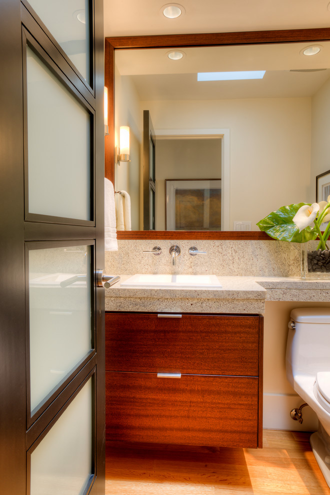 Inspiration for a small retro cloakroom in Seattle with flat-panel cabinets, dark wood cabinets, a one-piece toilet, beige tiles, stone tiles, beige walls, medium hardwood flooring, a built-in sink, granite worktops, brown floors and grey worktops.