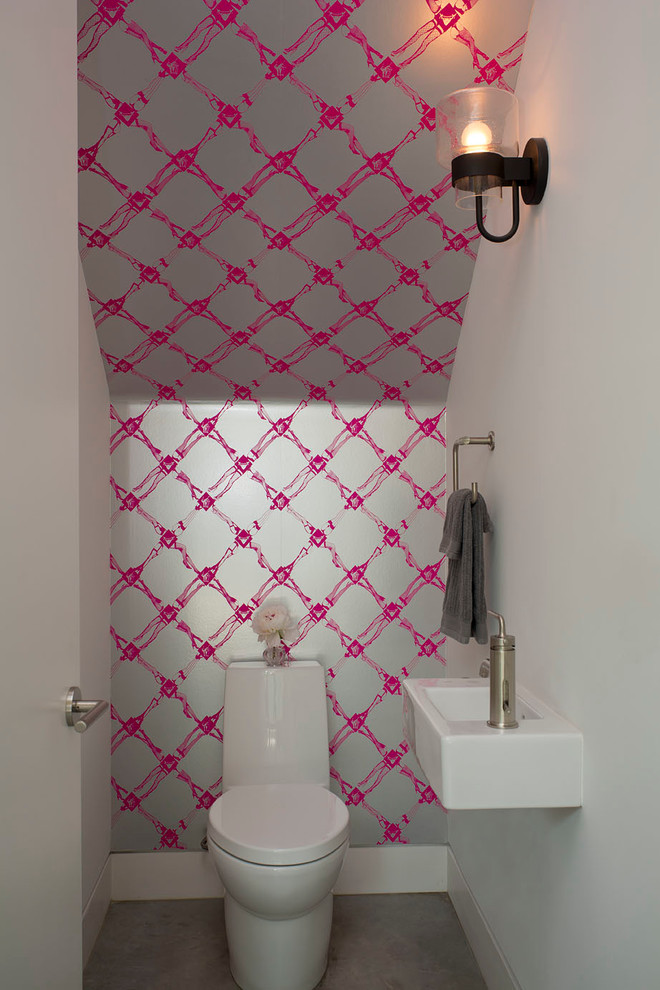 Inredning av ett modernt litet toalett, med ett väggmonterat handfat, en toalettstol med hel cisternkåpa, flerfärgade väggar och betonggolv