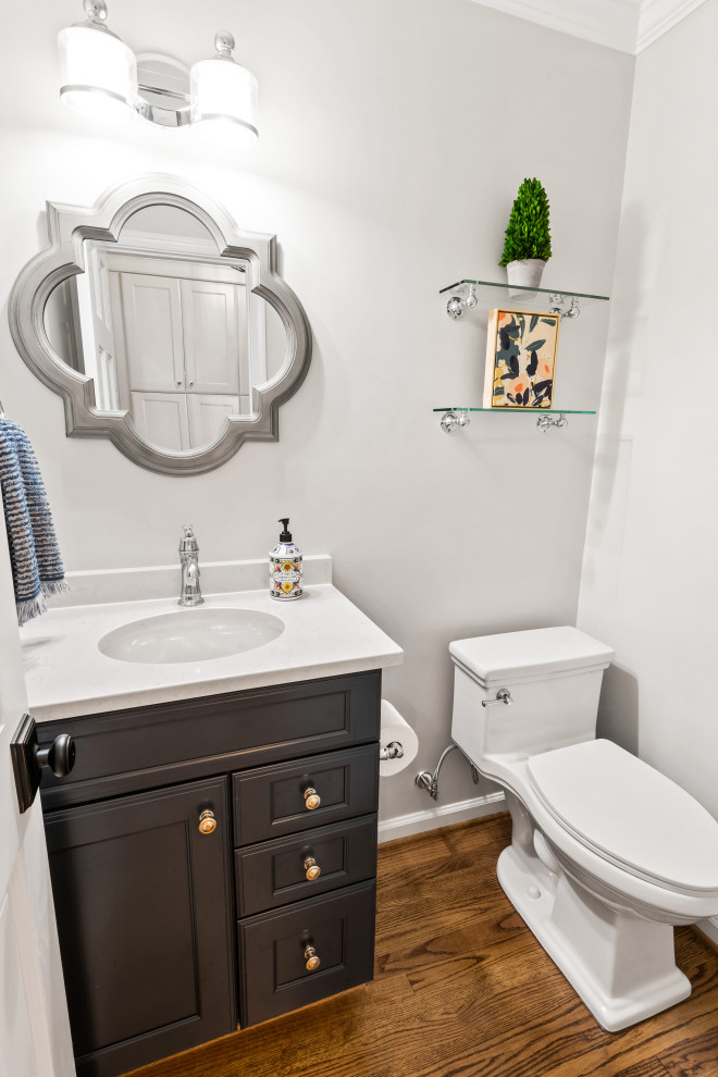 Cette photo montre un petit WC et toilettes bord de mer en bois foncé avec un placard à porte shaker, un mur gris, un sol en bois brun, un lavabo encastré, un plan de toilette en quartz modifié, un sol marron et un plan de toilette blanc.