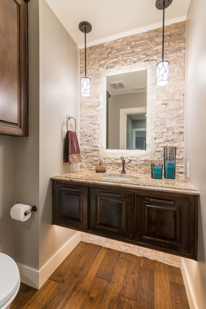 Example of a small transitional beige tile and stone tile medium tone wood floor powder room design in Austin with raised-panel cabinets, dark wood cabinets, a wall-mount toilet, gray walls, an undermount sink and granite countertops