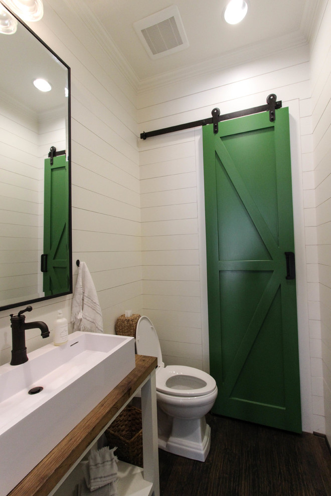 Bild på ett litet vintage brun brunt toalett, med ett avlångt handfat, träbänkskiva, vita väggar, mörkt trägolv och öppna hyllor