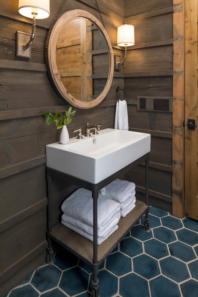 Bild på ett mellanstort rustikt toalett, med öppna hyllor, bruna skåp, en toalettstol med hel cisternkåpa, brun kakel, bruna väggar, klinkergolv i keramik, ett piedestal handfat, bänkskiva i akrylsten och blått golv