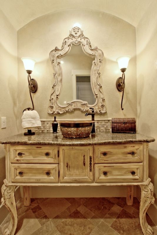 Powder room - mid-sized rustic beige tile and glass tile powder room idea in Austin with furniture-like cabinets, distressed cabinets, a two-piece toilet, beige walls, a vessel sink and granite countertops