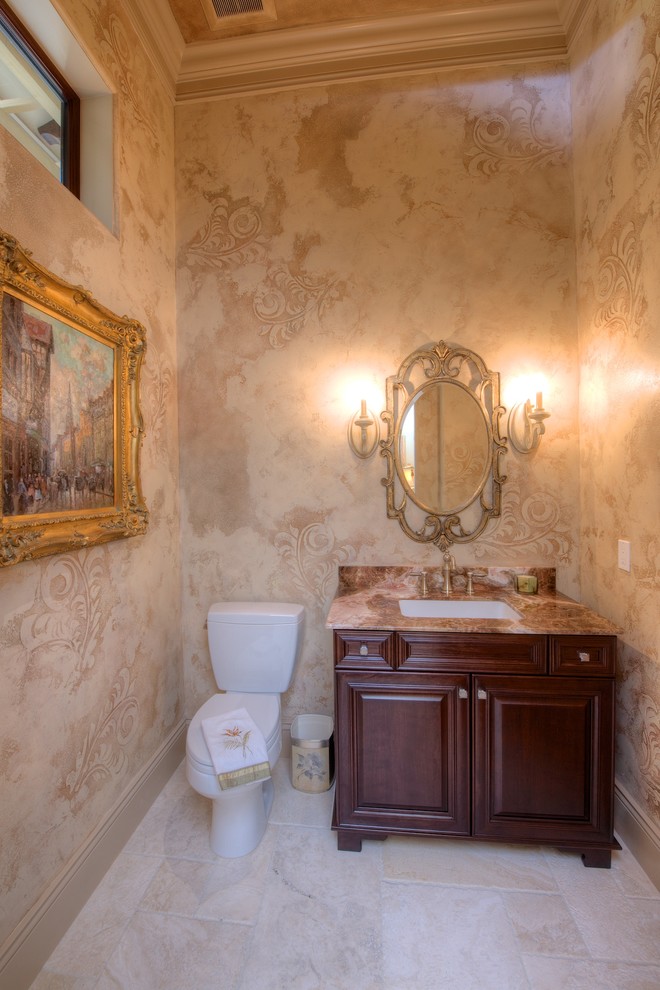 Inredning av ett klassiskt toalett, med ett undermonterad handfat, luckor med upphöjd panel, skåp i mörkt trä och beige kakel