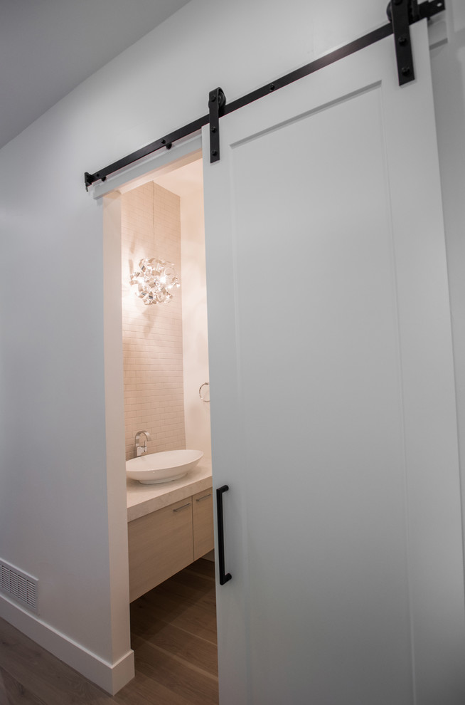 Photo of a medium sized modern cloakroom in Denver with flat-panel cabinets, light wood cabinets, a one-piece toilet, white tiles, metro tiles, white walls, light hardwood flooring, a vessel sink, engineered stone worktops and grey floors.