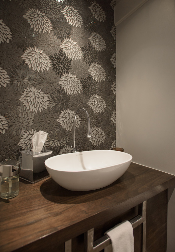 Idée de décoration pour un WC et toilettes minimaliste en bois brun de taille moyenne avec un placard à porte plane, mosaïque, un mur gris, une vasque et un plan de toilette en bois.