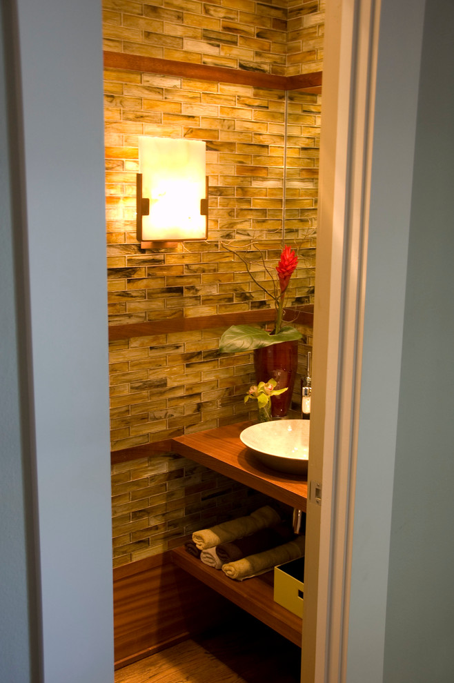 Kleine Moderne Gästetoilette mit Aufsatzwaschbecken, offenen Schränken, hellbraunen Holzschränken, Waschtisch aus Holz, braunen Fliesen, Glasfliesen, brauner Wandfarbe und braunem Holzboden in Dallas