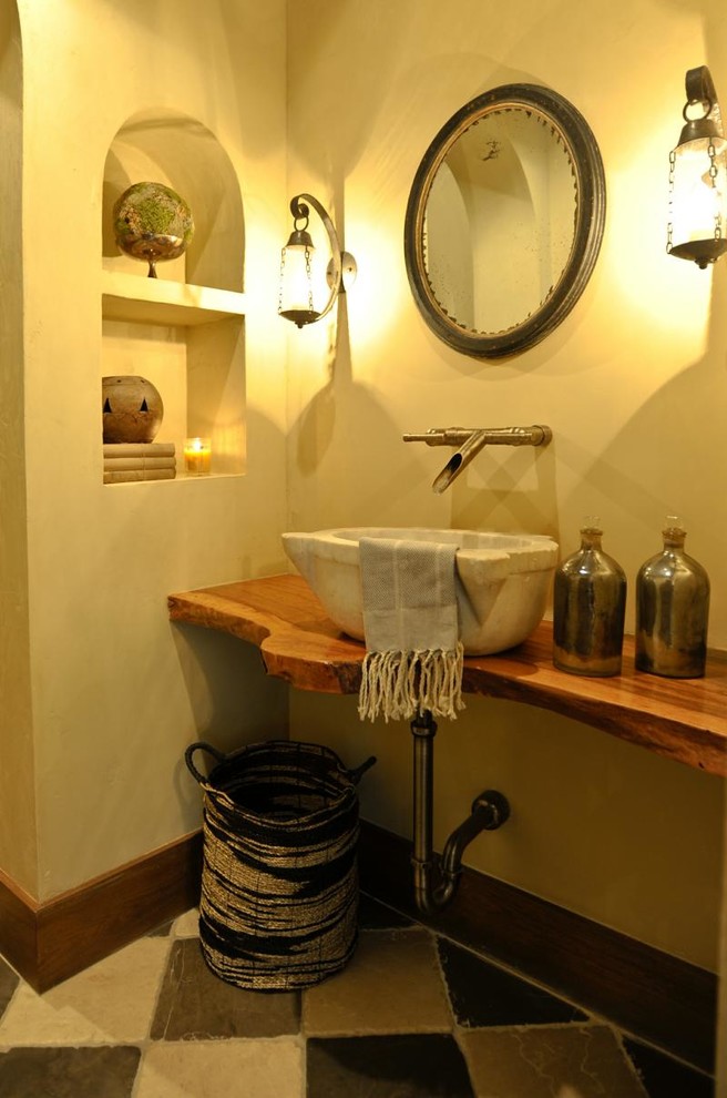 Пример оригинального дизайна: туалет среднего размера в стиле рустика с настольной раковиной, столешницей из дерева, разноцветной плиткой, бежевыми стенами, полом из цементной плитки и коричневой столешницей
