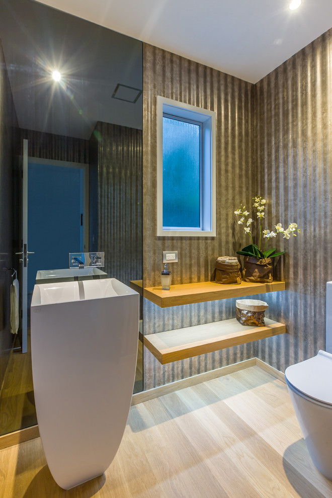Exempel på ett litet industriellt toalett, med öppna hyllor, skåp i ljust trä, en toalettstol med separat cisternkåpa, bruna väggar, ljust trägolv, ett piedestal handfat och träbänkskiva