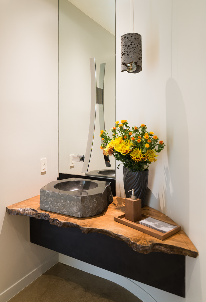 Inspiration for a mid-sized contemporary concrete floor powder room remodel in Los Angeles with a one-piece toilet, beige walls, a vessel sink and wood countertops