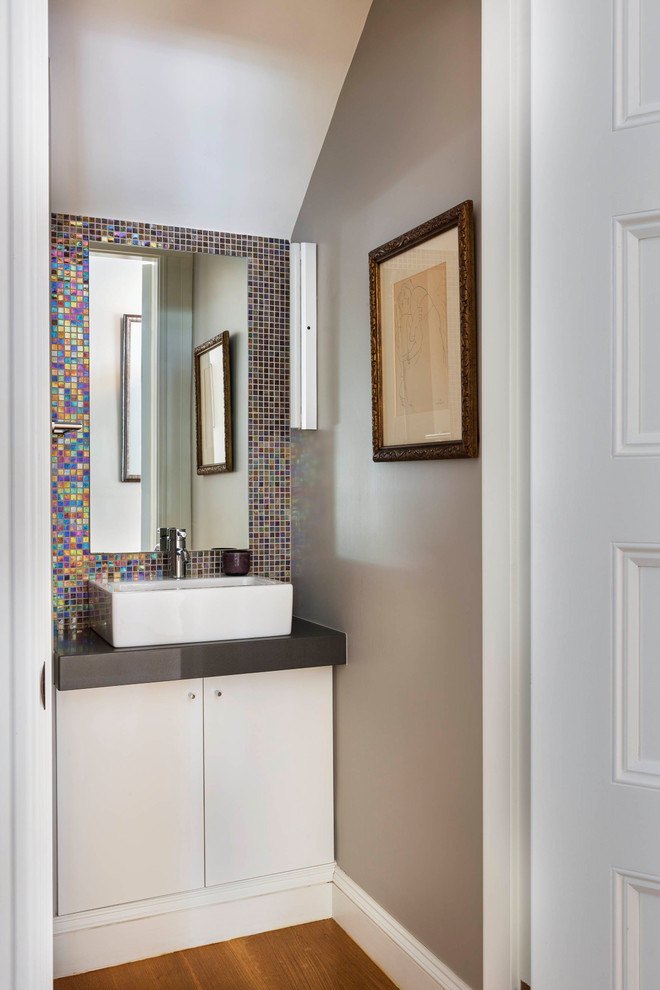Modern inredning av ett litet toalett, med släta luckor, vita skåp, flerfärgad kakel, keramikplattor, grå väggar, ljust trägolv, ett fristående handfat och bänkskiva i kvarts