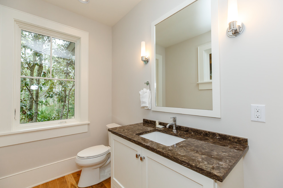 Bild på ett mellanstort maritimt brun brunt toalett, med skåp i shakerstil, vita skåp, en toalettstol med separat cisternkåpa, grå väggar, mellanmörkt trägolv, ett undermonterad handfat, marmorbänkskiva och brunt golv