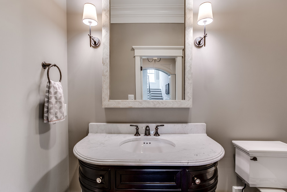 Example of a mid-sized transitional medium tone wood floor powder room design in DC Metro with furniture-like cabinets, dark wood cabinets, a two-piece toilet, beige walls, an integrated sink and marble countertops