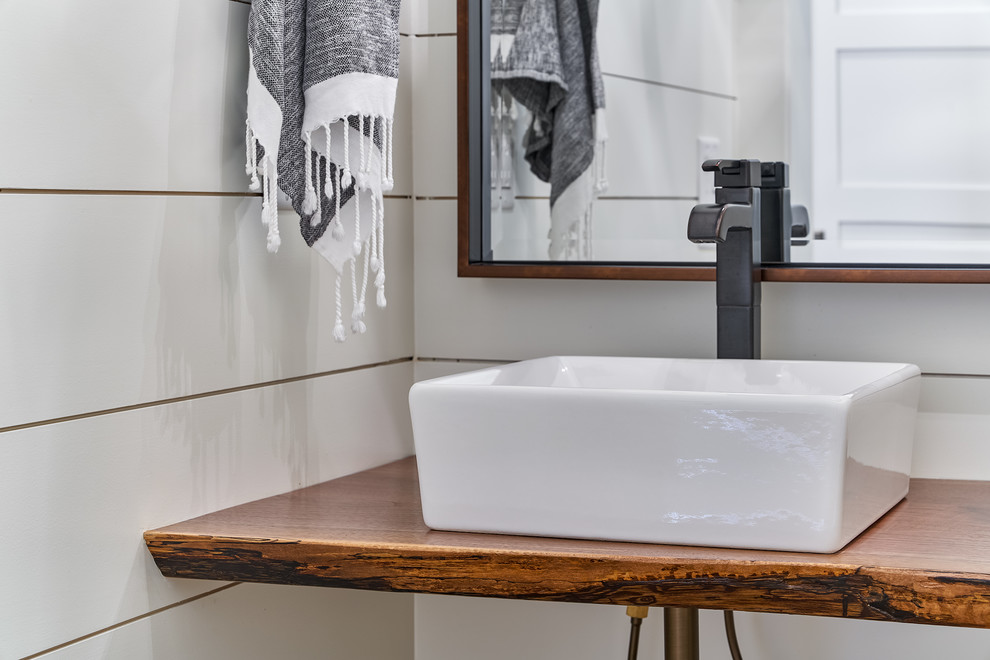 Diseño de aseo marinero con paredes blancas, suelo de madera en tonos medios, lavabo sobreencimera, encimera de madera y suelo marrón