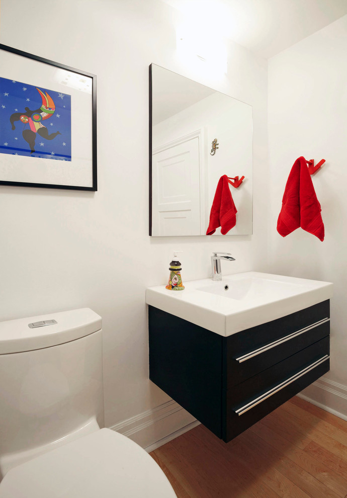 Small modern cloakroom in Toronto with a one-piece toilet, white walls, flat-panel cabinets, black cabinets, medium hardwood flooring, an integrated sink, quartz worktops and brown floors.