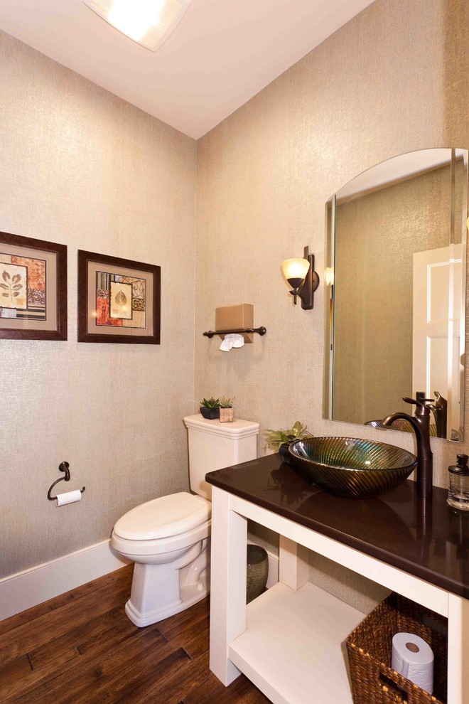 Lantlig inredning av ett litet brun brunt toalett, med öppna hyllor, vita skåp, en toalettstol med separat cisternkåpa, beige väggar, mörkt trägolv, ett fristående handfat, granitbänkskiva och brunt golv